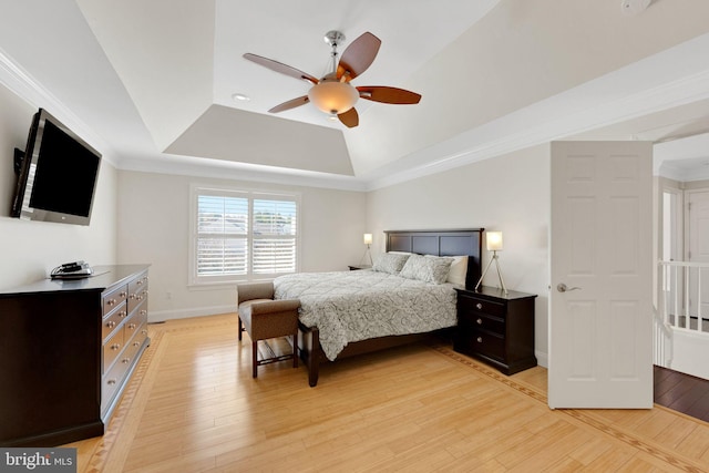 bedroom with ornamental molding, a tray ceiling, light wood finished floors, baseboards, and ceiling fan