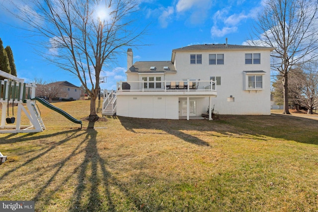 rear view of house with a lawn, a chimney, a deck, a playground, and stairs