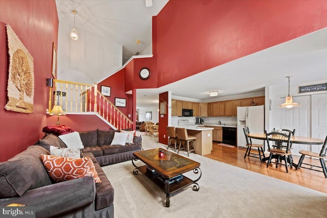 living room with a high ceiling, stairway, and light wood-type flooring