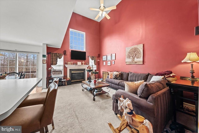 carpeted living area featuring a towering ceiling, ceiling fan, and a glass covered fireplace