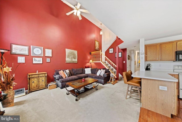 living room featuring a ceiling fan, light colored carpet, a high ceiling, and stairs