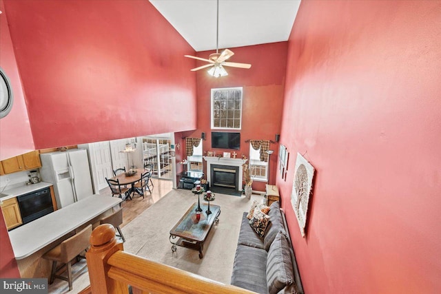 living room with high vaulted ceiling, a glass covered fireplace, wood finished floors, and a ceiling fan