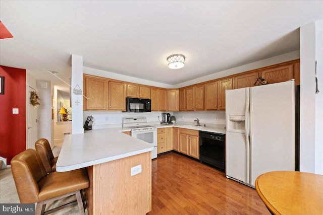 kitchen with wood finished floors, a peninsula, light countertops, black appliances, and a sink