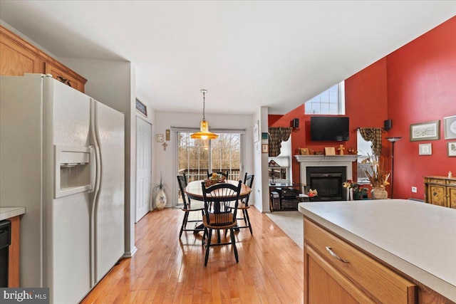 kitchen featuring white fridge with ice dispenser, light countertops, hanging light fixtures, and light wood finished floors