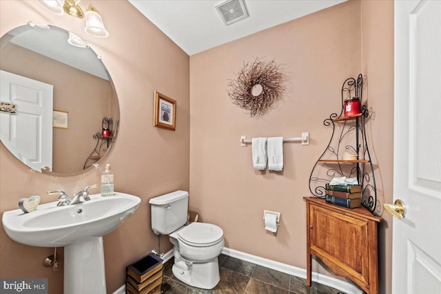 half bathroom with toilet, visible vents, baseboards, and a sink