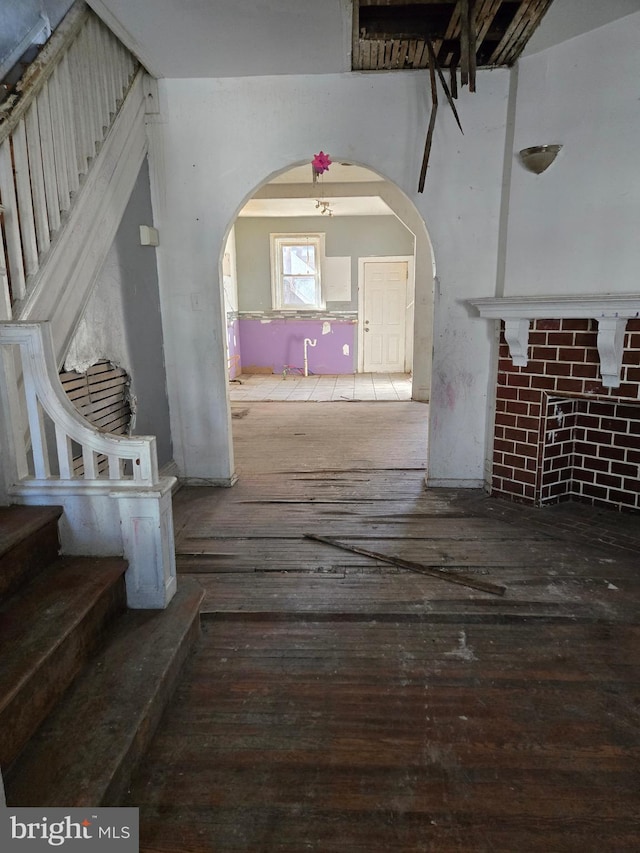 unfurnished living room featuring arched walkways, stairway, and hardwood / wood-style floors