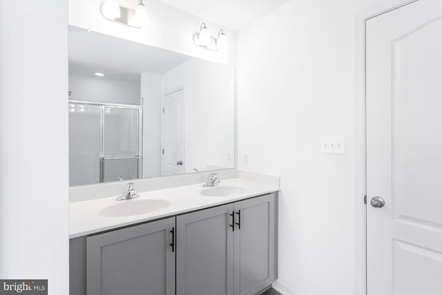 full bath featuring double vanity, a sink, and a shower with door