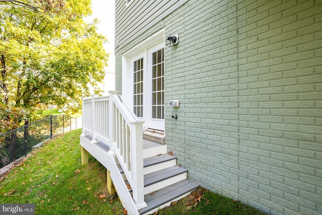 property entrance featuring brick siding, fence, a wooden deck, and a lawn