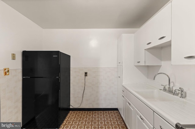 kitchen featuring freestanding refrigerator, white cabinetry, a sink, and tile walls