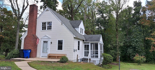 view of front of property featuring a shingled roof, a sunroom, and a front lawn