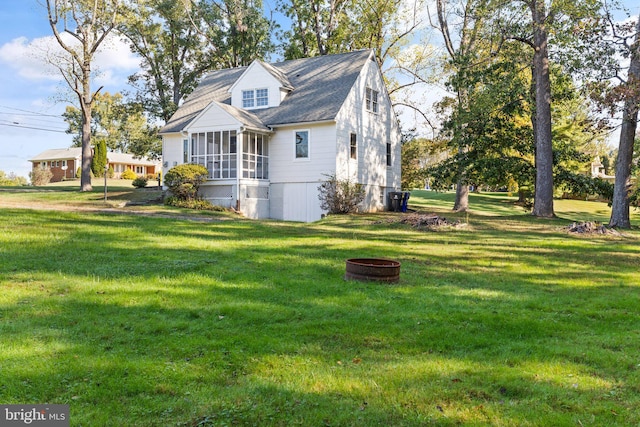 view of property exterior featuring a yard, an outdoor fire pit, and a sunroom