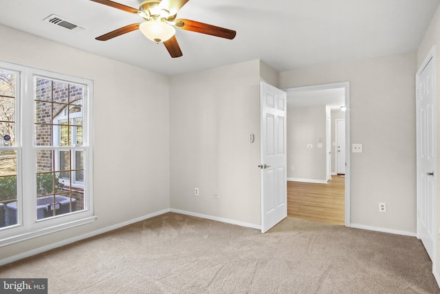 spare room featuring light colored carpet, visible vents, ceiling fan, and baseboards