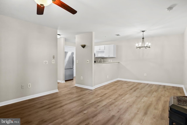 unfurnished living room with a sink, baseboards, wood finished floors, and ceiling fan with notable chandelier