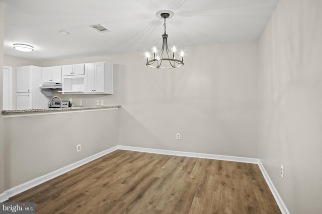 unfurnished dining area with an inviting chandelier, visible vents, baseboards, and wood finished floors