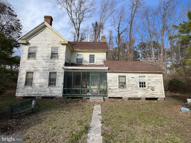 view of front facade featuring a sunroom, a chimney, and a front lawn