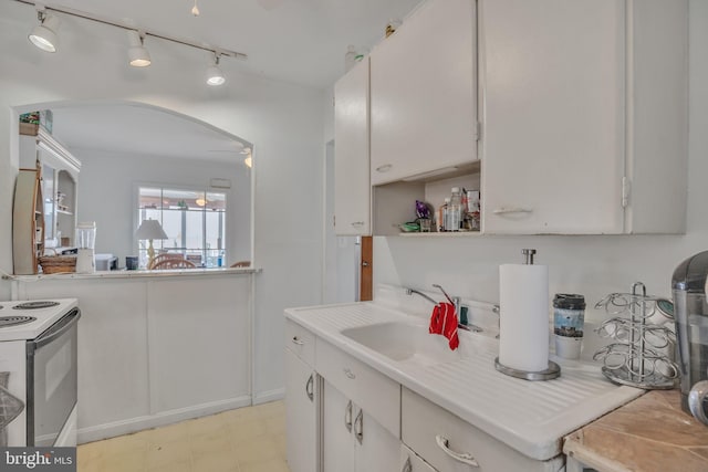 kitchen featuring white electric range oven, arched walkways, white cabinets, light countertops, and a sink