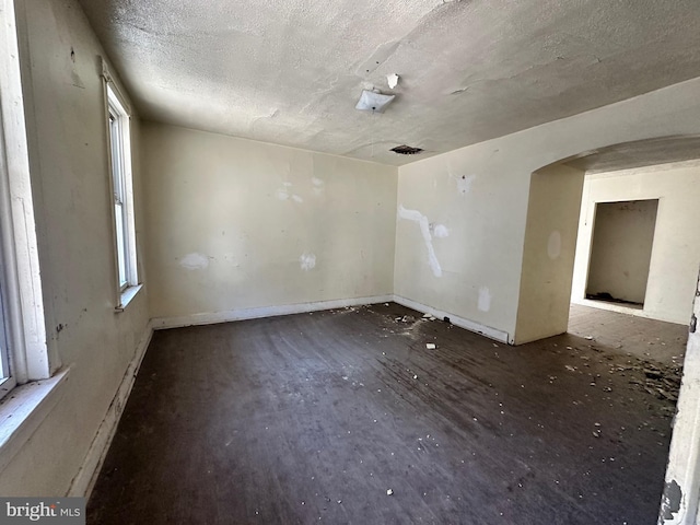 spare room featuring a healthy amount of sunlight, arched walkways, and a textured ceiling