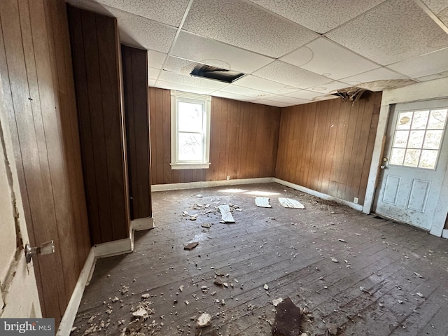 unfurnished room featuring a drop ceiling, wood walls, and baseboards