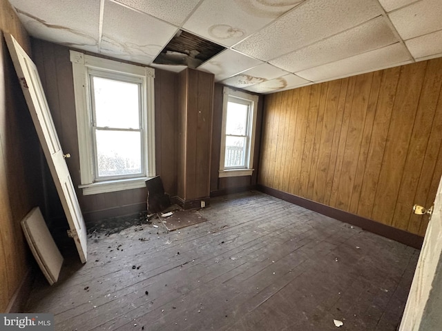 empty room featuring a paneled ceiling, hardwood / wood-style floors, wooden walls, and a wealth of natural light