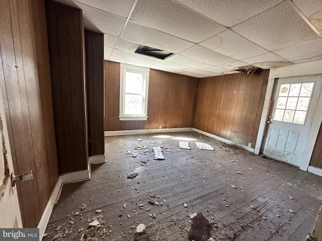 empty room featuring a paneled ceiling, wood walls, and baseboards