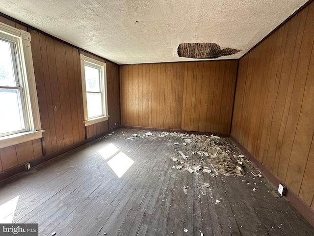 unfurnished room featuring baseboards, wood walls, a textured ceiling, and hardwood / wood-style floors