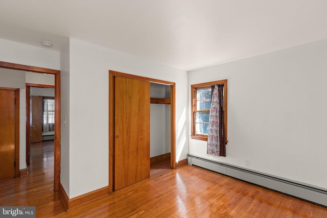 unfurnished bedroom featuring a baseboard heating unit, a closet, baseboards, and wood finished floors