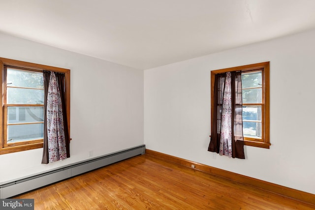 empty room with a baseboard heating unit, a healthy amount of sunlight, light wood-style floors, and baseboards