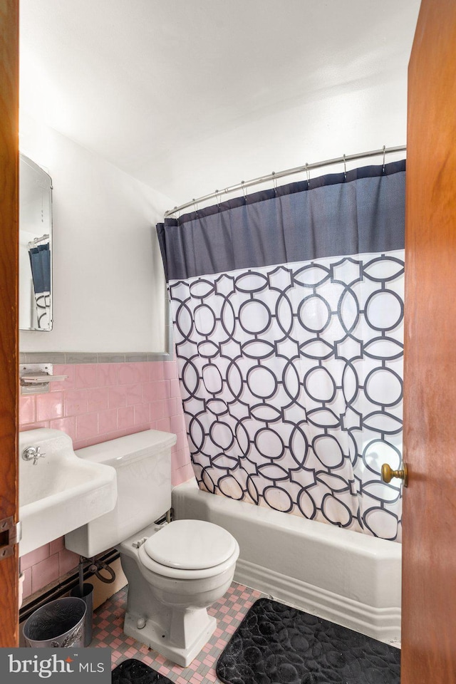 bathroom with a wainscoted wall, tile walls, toilet, and shower / bath combo with shower curtain