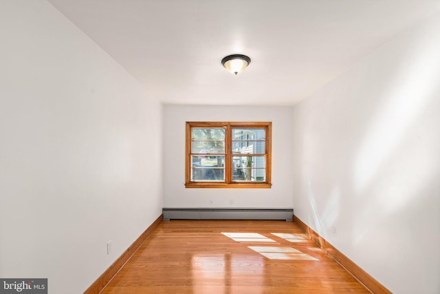 empty room with a baseboard heating unit, light wood-type flooring, and baseboards