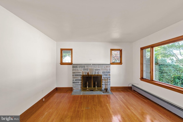 unfurnished living room featuring a baseboard heating unit, a stone fireplace, light wood-type flooring, and baseboards