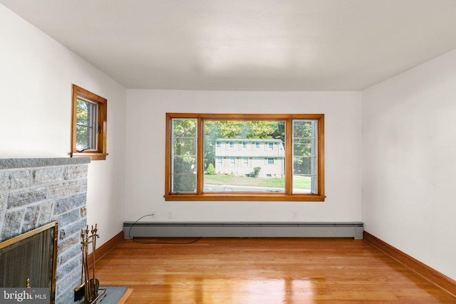 living room with a stone fireplace, baseboard heating, light wood-type flooring, and a wealth of natural light