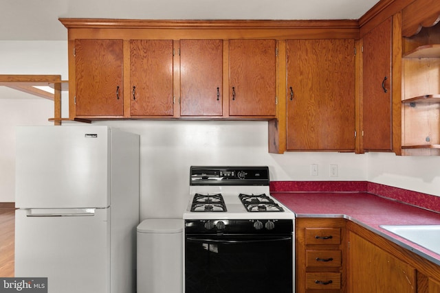 kitchen featuring brown cabinetry, freestanding refrigerator, a sink, and gas stove