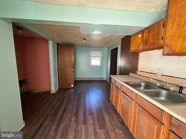 kitchen with a textured ceiling, a baseboard heating unit, a sink, brown cabinets, and dark wood-style floors