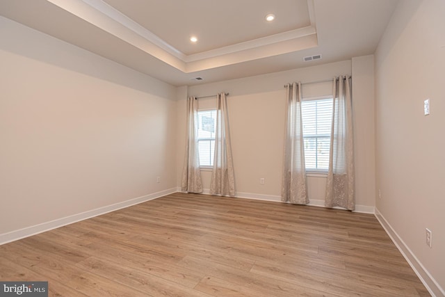 empty room with light wood-style flooring, visible vents, and a raised ceiling