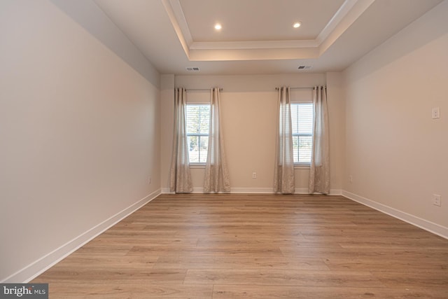 unfurnished room with light wood finished floors, baseboards, visible vents, and a raised ceiling