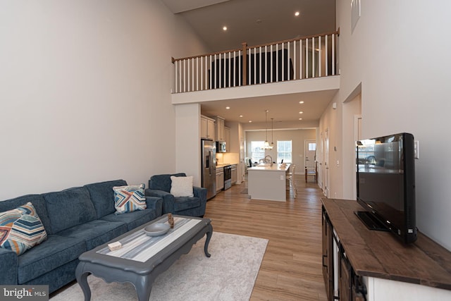 living area featuring a towering ceiling, light wood-style flooring, and recessed lighting