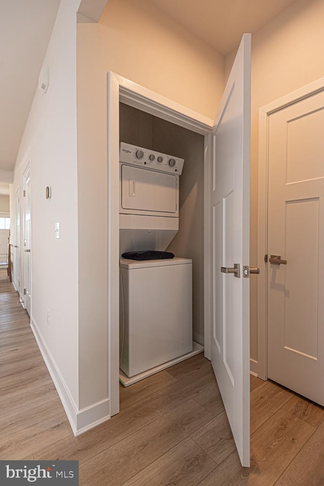 washroom with stacked washer and dryer, wood finished floors, laundry area, and baseboards