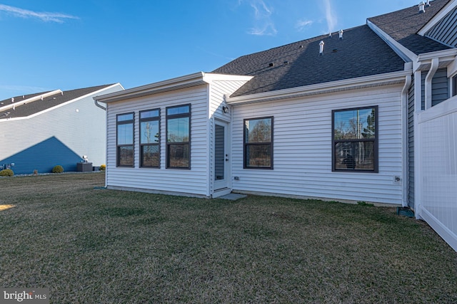 rear view of property featuring a shingled roof, cooling unit, and a yard