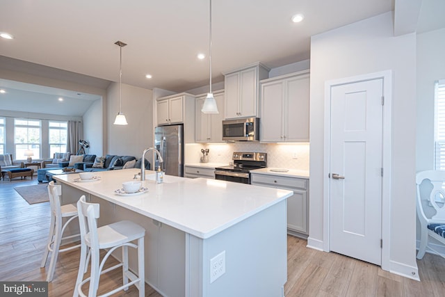 kitchen with light wood-style flooring, appliances with stainless steel finishes, open floor plan, a kitchen bar, and backsplash