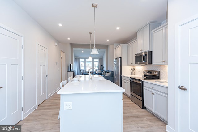 kitchen with appliances with stainless steel finishes, light wood-type flooring, a center island with sink, and decorative backsplash