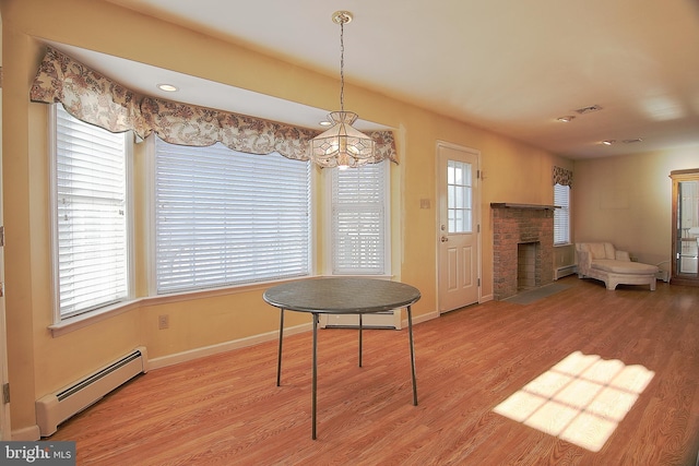 dining room with baseboard heating, a brick fireplace, and light wood-style flooring