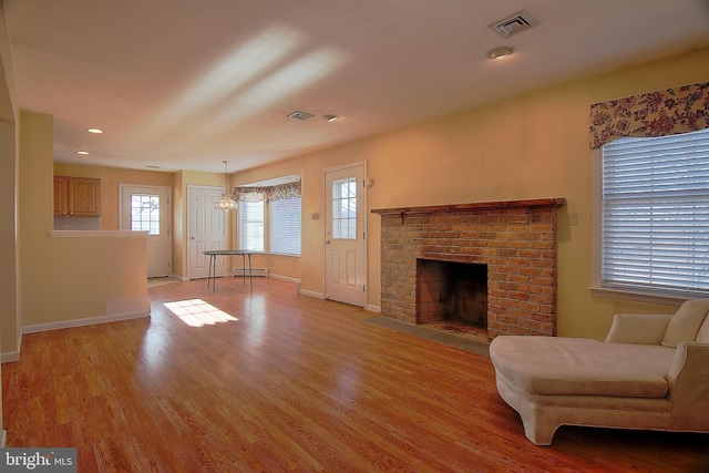 living room featuring a baseboard heating unit, a brick fireplace, visible vents, and light wood-style flooring