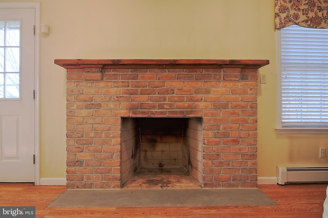 room details featuring a brick fireplace, baseboards, a baseboard heating unit, and wood finished floors