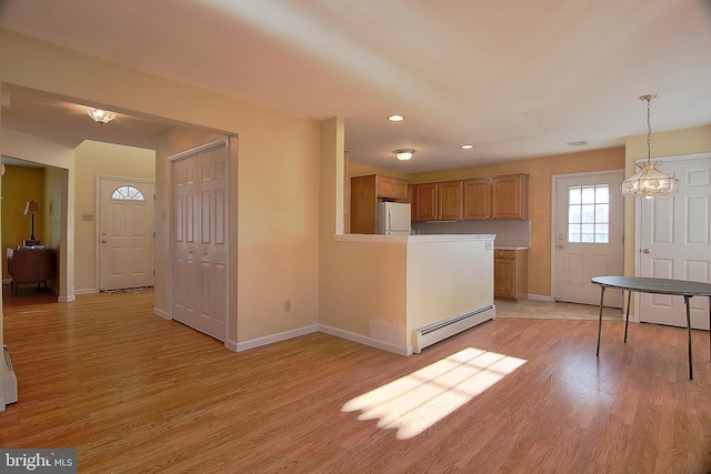 kitchen featuring light wood finished floors, a baseboard heating unit, brown cabinetry, and freestanding refrigerator