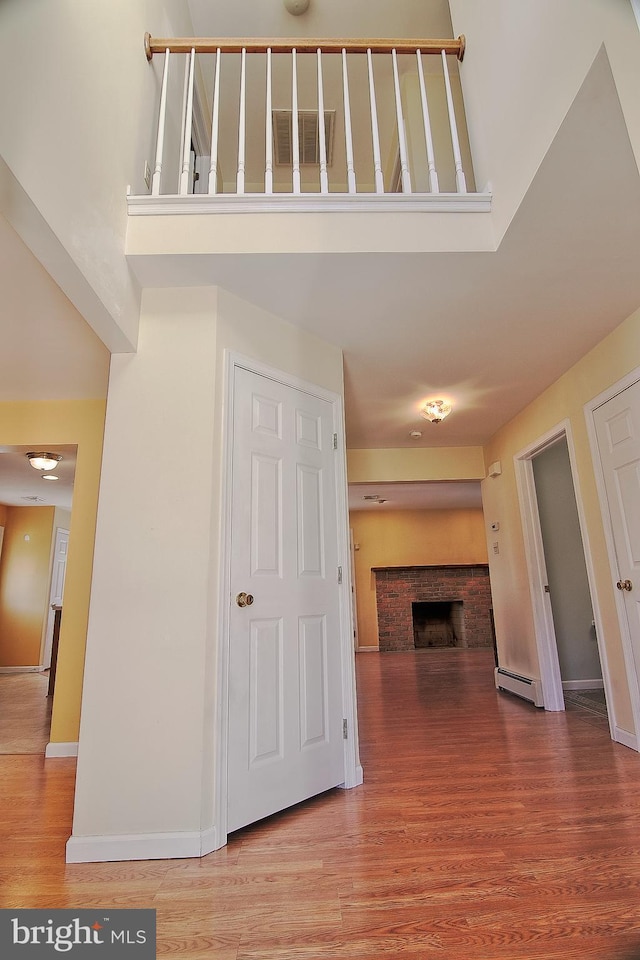 hallway with a high ceiling, a baseboard radiator, wood finished floors, and baseboards