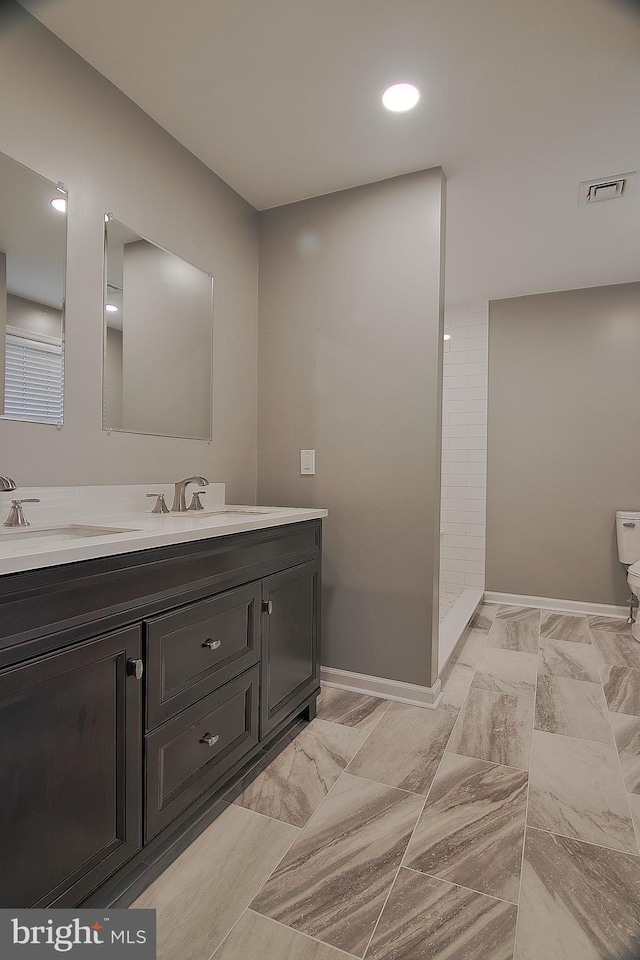 full bathroom with double vanity, visible vents, a tile shower, and a sink