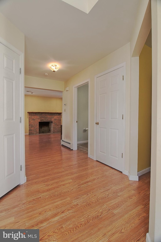 corridor featuring baseboard heating, light wood-style flooring, and baseboards