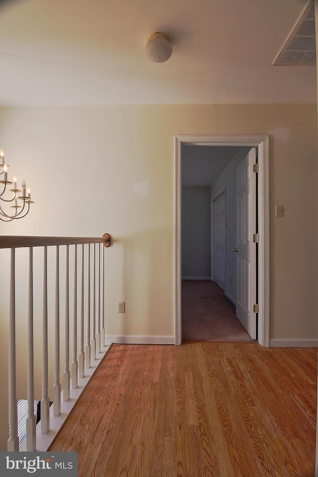 hallway with baseboards, a notable chandelier, visible vents, and wood finished floors