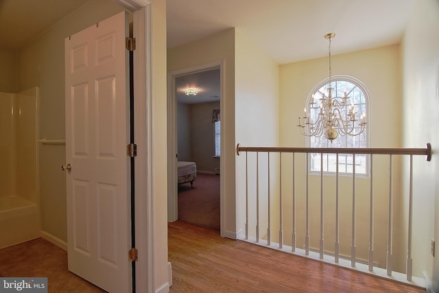 corridor with baseboards, wood finished floors, and an inviting chandelier