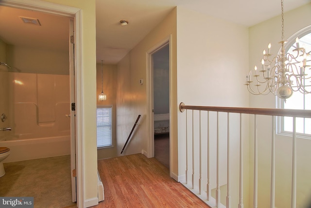 corridor featuring visible vents, wood finished floors, a notable chandelier, and an upstairs landing